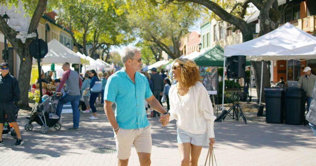 a man and woman holding hands and walking at the Bradenton Market