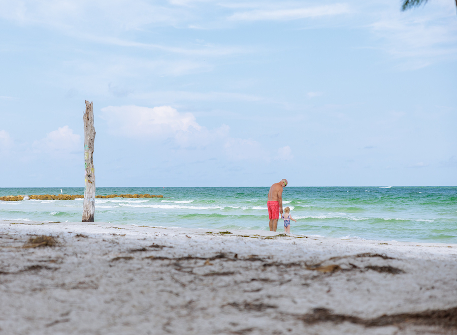 grandfather and small child holding hands on the shore of Beer Can Island
