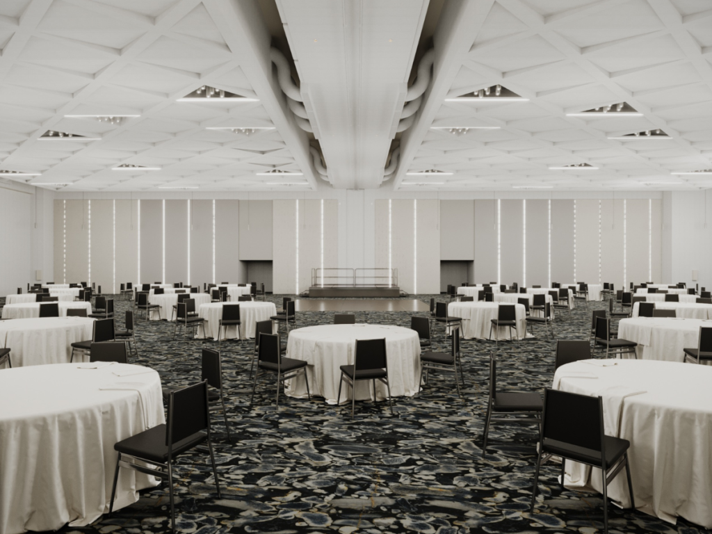 A rendered image of a large ballroom is filled with round cloth-covered round tables with chairs as well as a dancefloor and stage in the center of the back wall, depicting the incredible renovations made to the Bradenton Area Convention Center in Florida's Gulf Coast.