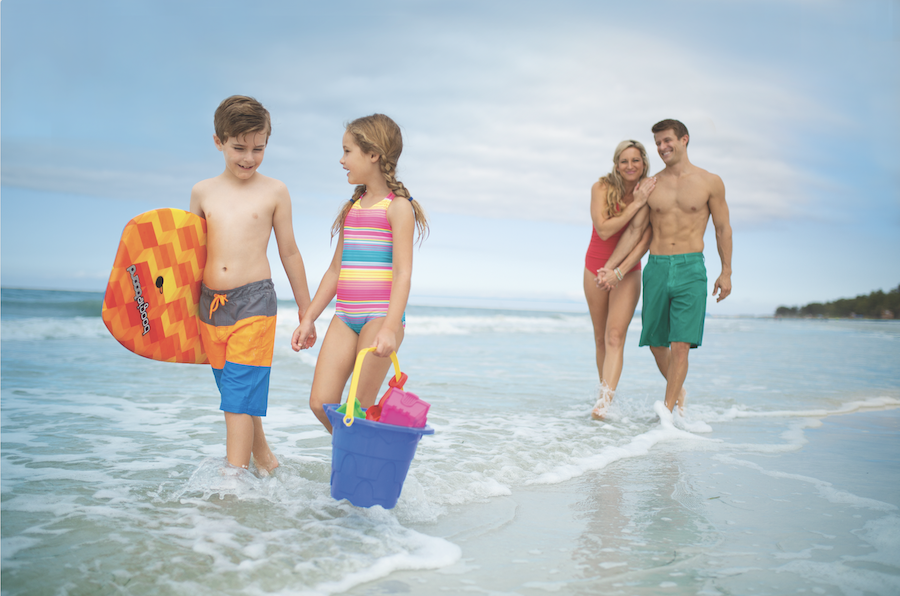 family of four wading in the waves on a beach